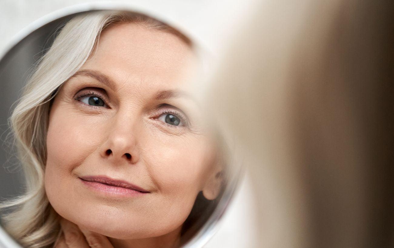 This is a picture of a woman looking at her face and skin in the mirror