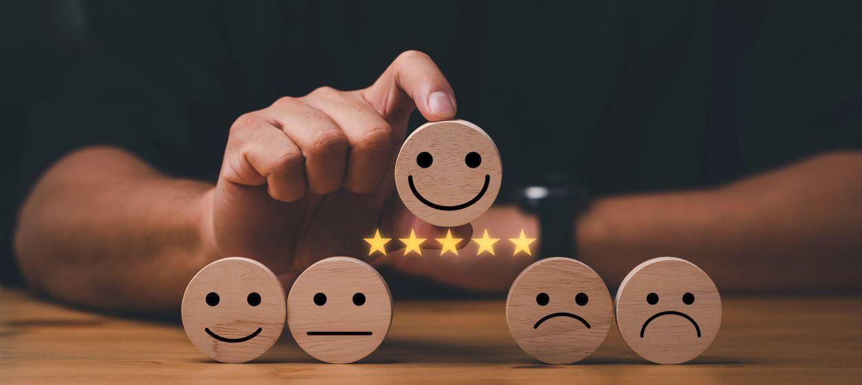 This is a picture of real life happy emojis with a 5 star happy face emoji on top, held up by a mans fingertips.