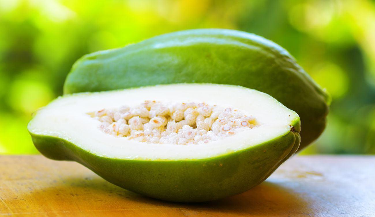 This is a picture of an unripe green papaya on a wood table with a green background