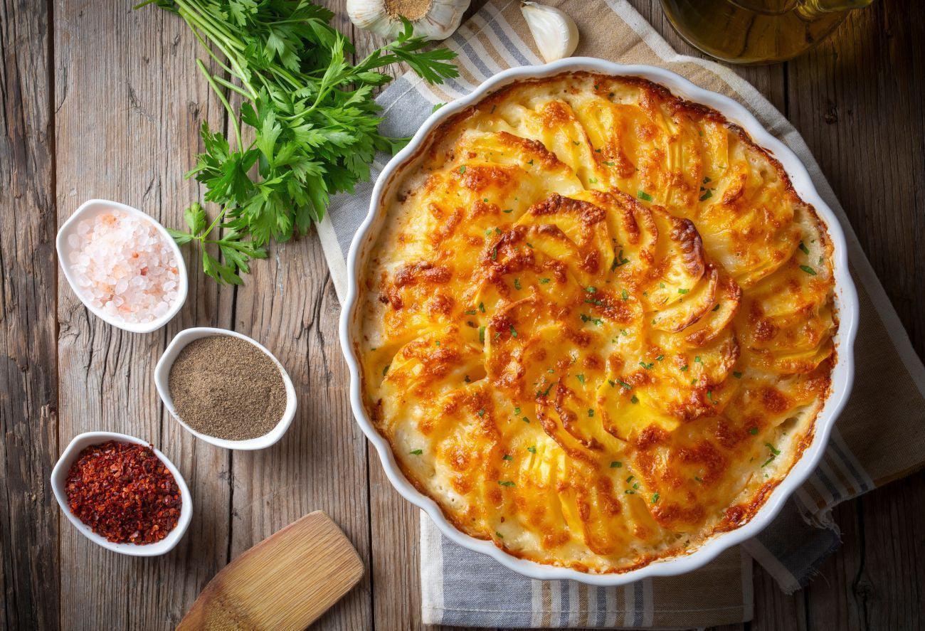 This is a picture of a scalloped potatoes casserole on a wooden table with some spices next to it