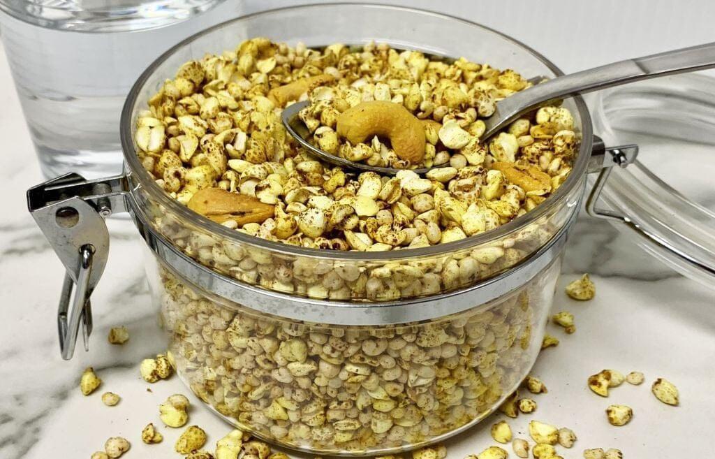 This is a picture of grains in a glass jar with a spoon inside, on a white table top.