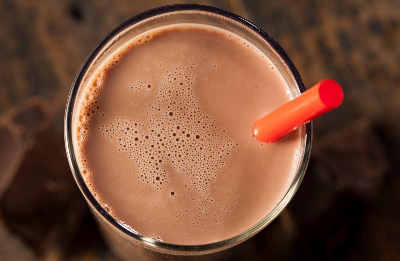 This is a picture of a glass of chocolate milk with a red straw on a wooden table