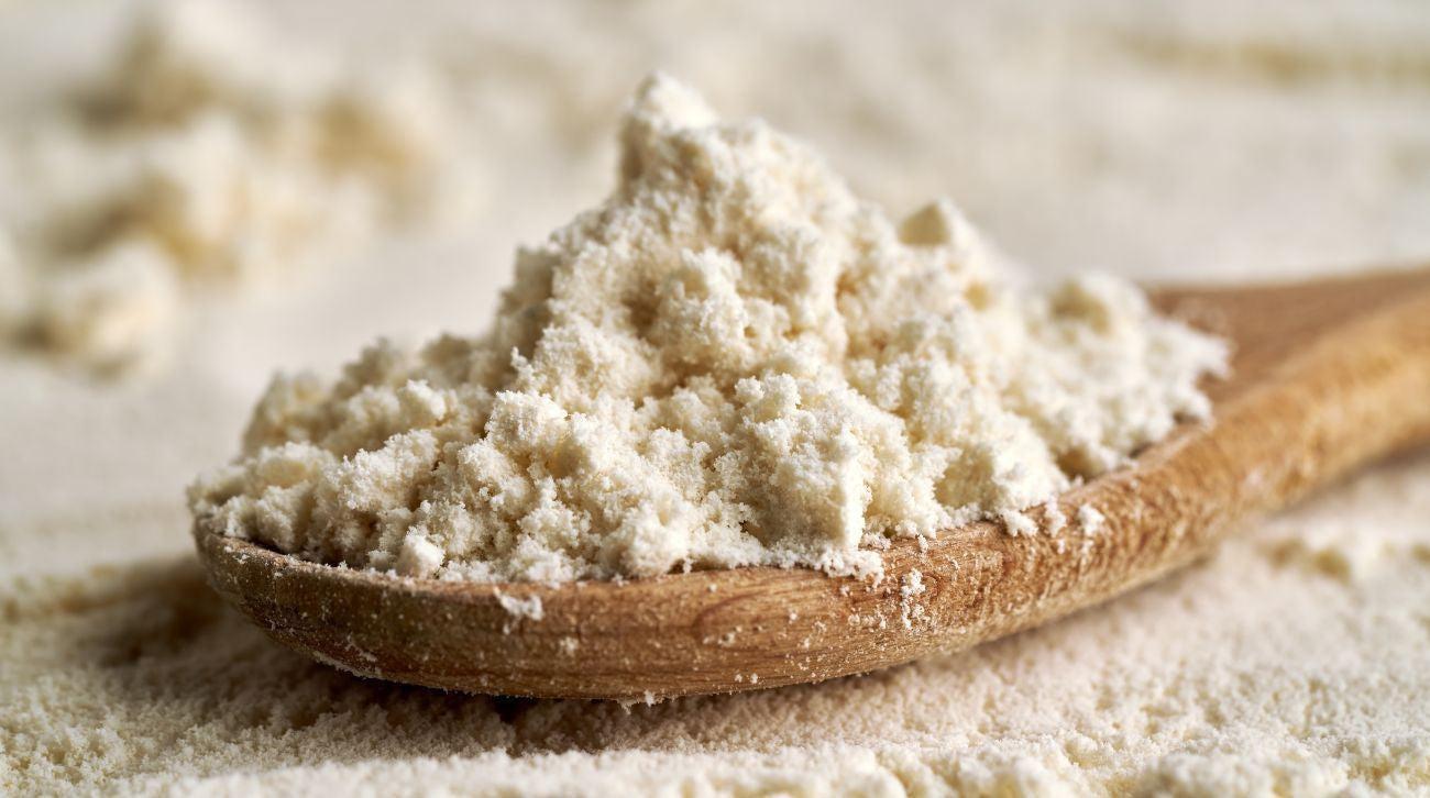 This is a picture of whey protein concentrate on a wooden spoon with a background that has more protein powder