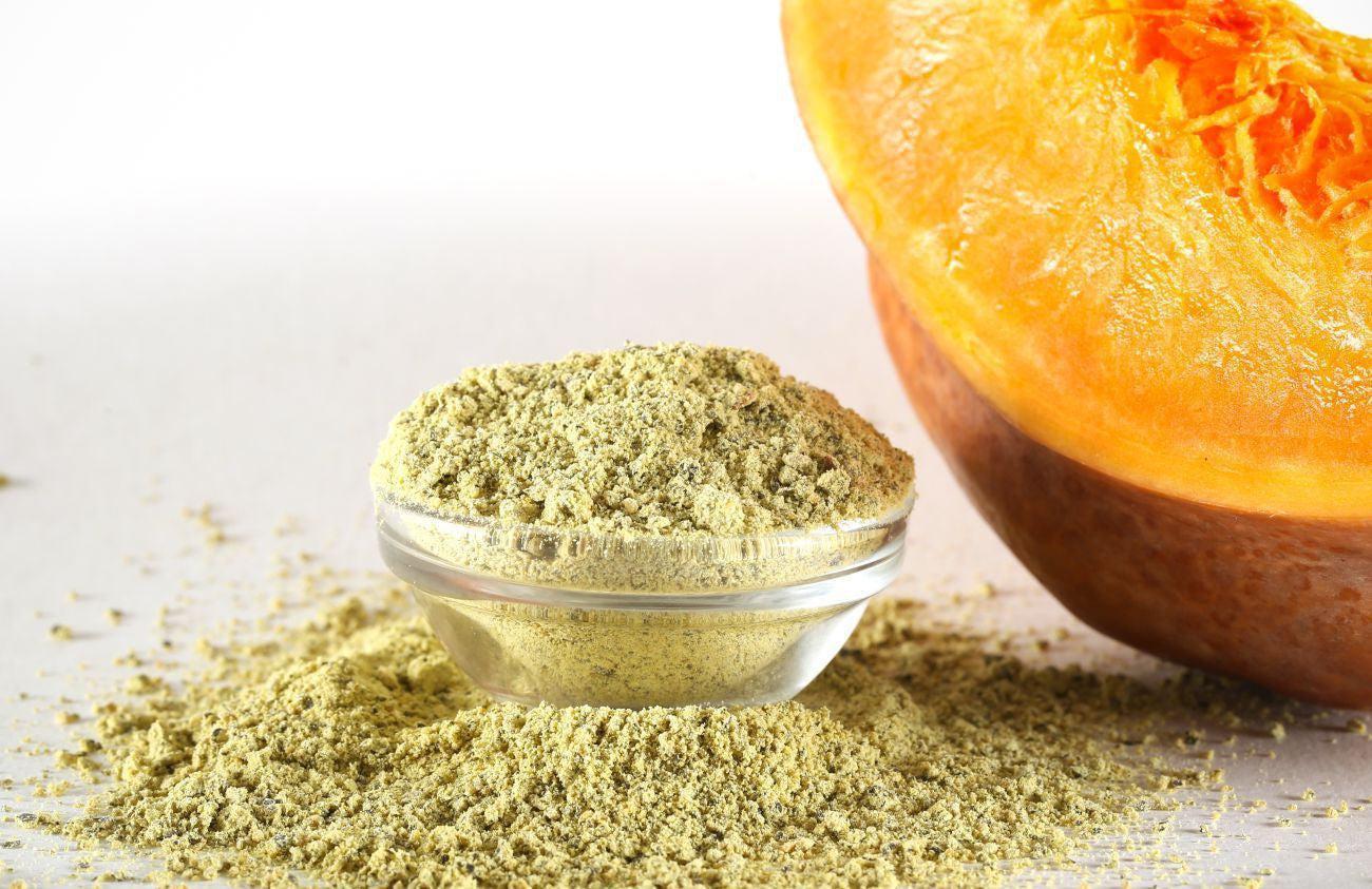 This is a picture of fresh pumpkin with a glass bowl of pumpkin protein powder on a white background