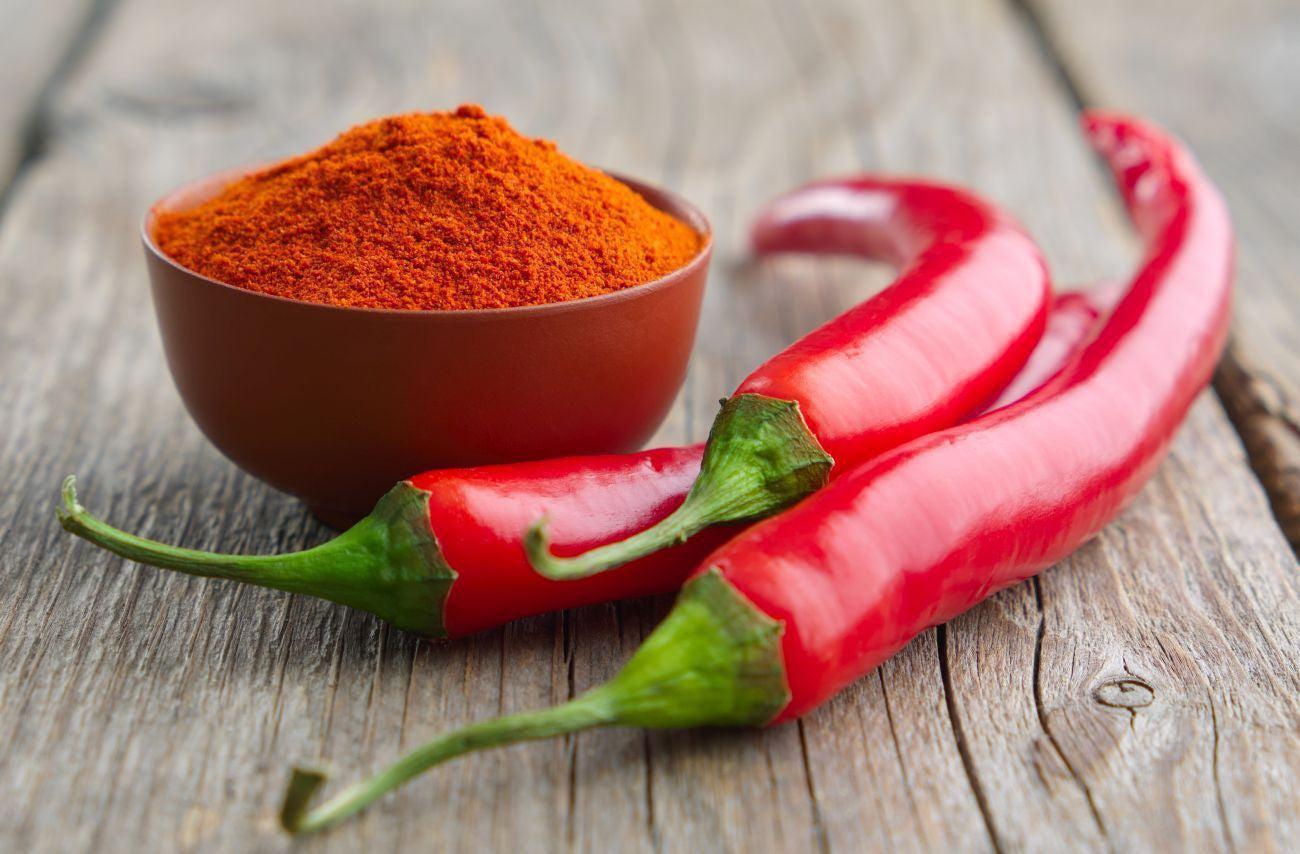 This is a picture of two cayenne peppers with a red bowl filled with cayenne powder, on a wooden background