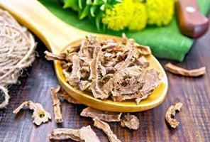 This is a picture of dried herbs on a wooden spoon, laying on a wooden table.