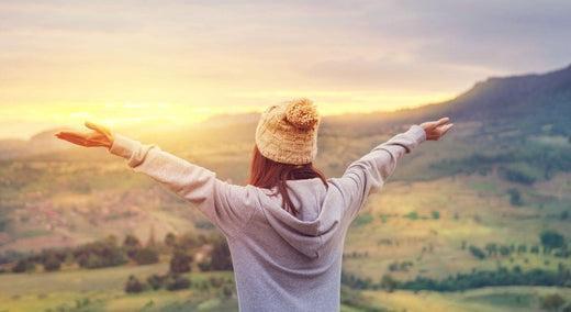 This is a picture of a stress-free woman overlooking the sunset and mountains across a valley.