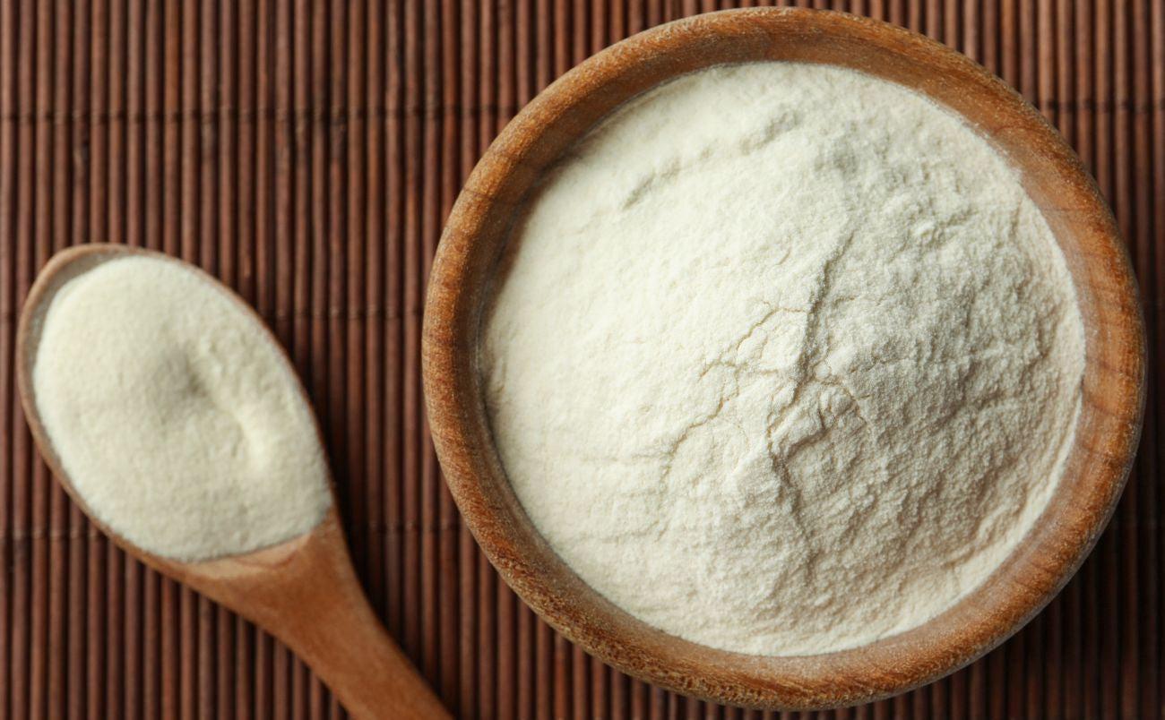 This is a picture of collagen powder in a wooden bowl with a wooden spoon on a wooden background