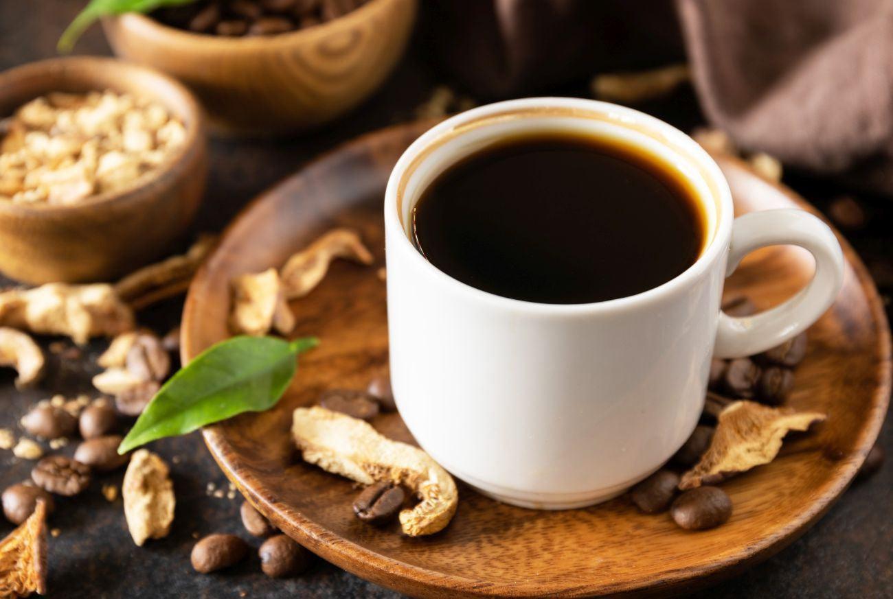 This is a picture of mushroom coffee in a white cup, on a wooden plate and on a wooden table with elegant mushrooms and decorations