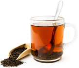 Assam Tea leave laying in wooden scoop and tea is made in glass cup with spoon.