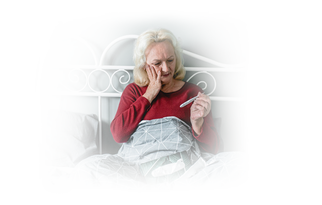Image of woman sitting up in bed looking down at the temperature reading on the thermometer.