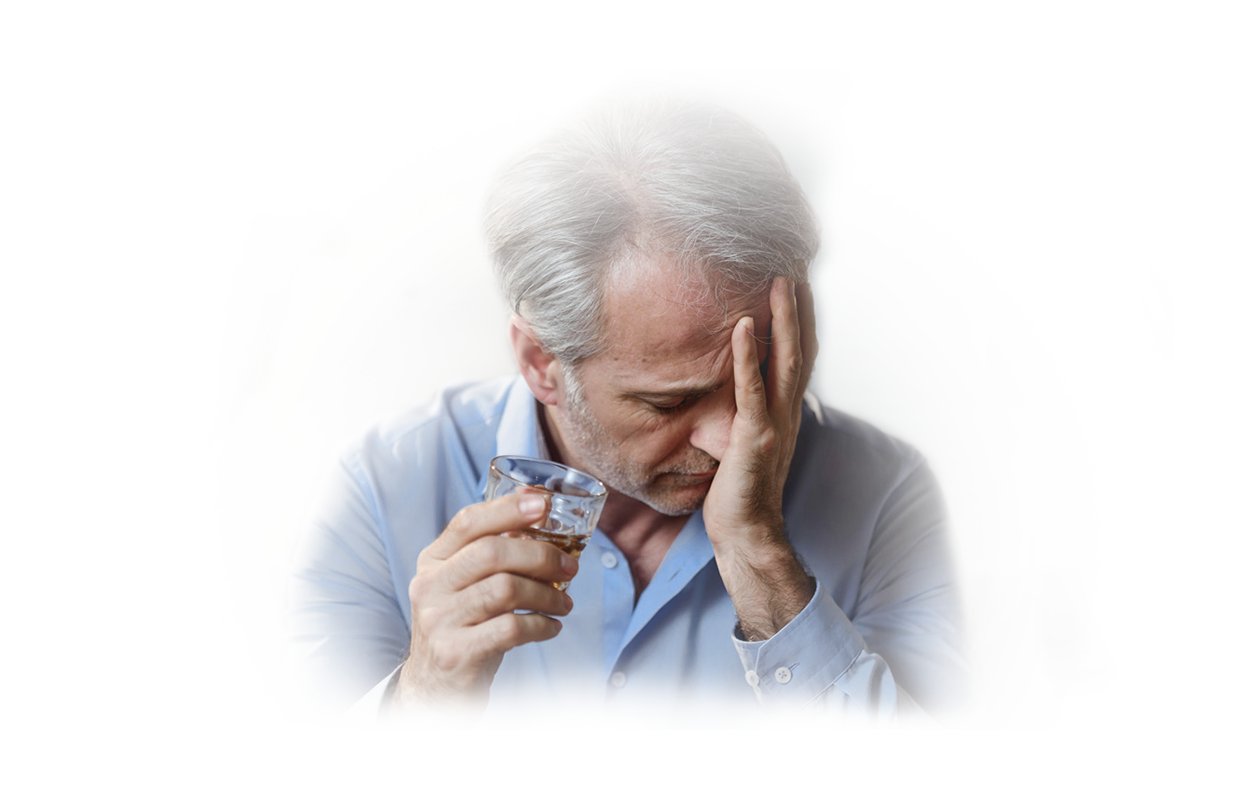Image of groggy man with hand on his face holding a shot of whiskey in his other hand.