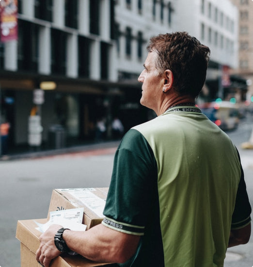 Guy holding several boxed on city street with building in background