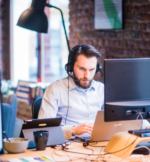 Guy wearing headphones sitting at desk with laptop and tablet