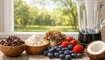This is a picture of fresh dark chocolate in a wooden bowl, whey protein powder, maitake mushroom, blueberries and strawberries, fresh coconut half and a blender on a kitchen counter with an open window overlooking a nice backyard