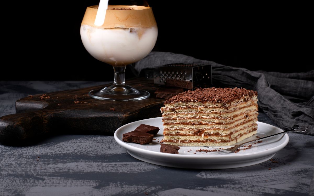 This is a picture of our Dalgona Dark Chocolate Coffee Cake on a white plate, topped with a checkerboard pattern of dark chocolate.