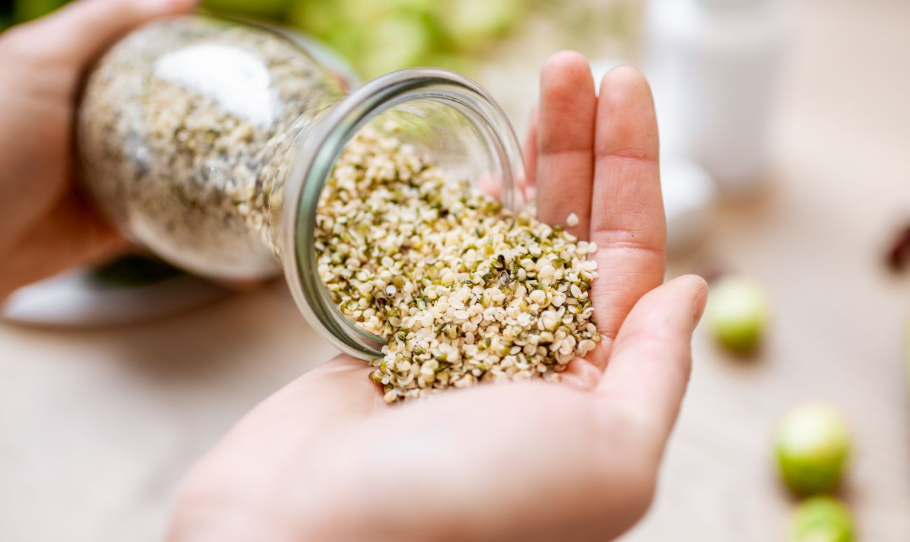 This is a picture of help seeds being poured from a glass jar into an open hand with a blurred out background.