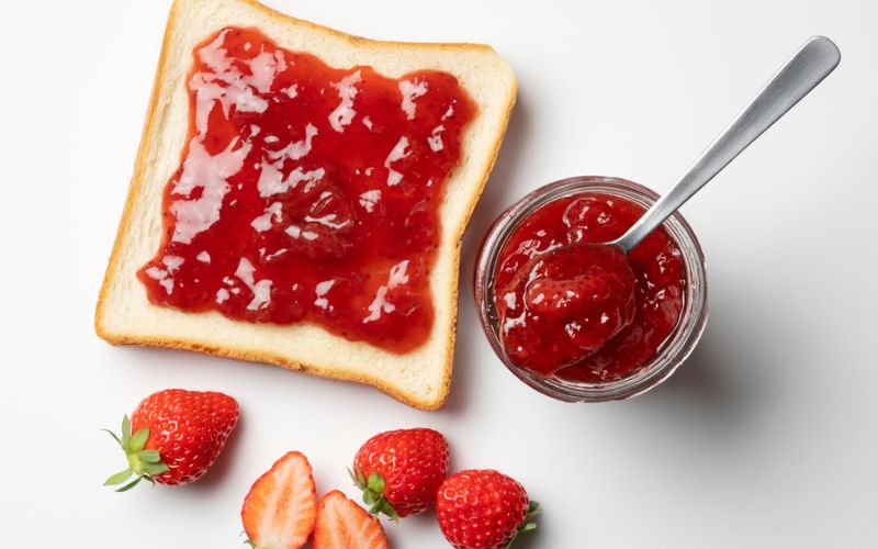 This is a picture of our Homemade Strawberry - Raspberry Jam on fresh bread with a glass bowl on a white background.