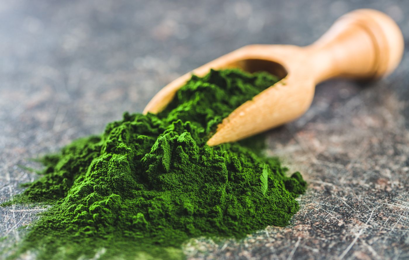 This is a picture of a dark green powder using a wooden spoon on a wood table