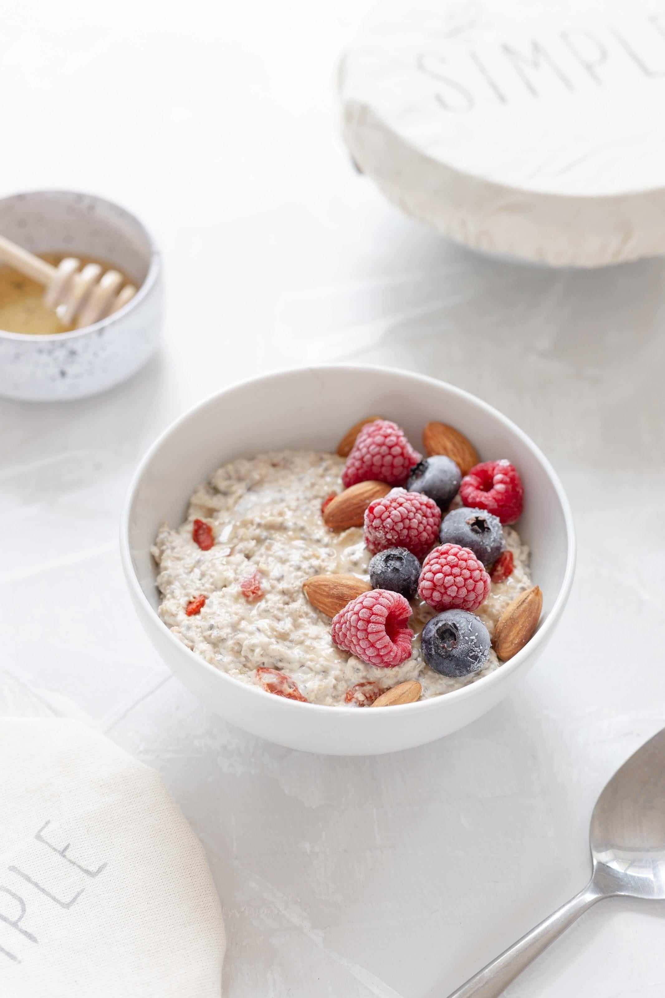 This is a picture of mixed berrys on a bowl of oatmeal in a white bowl, with honey and a bowl of milk all sitting on a white counter