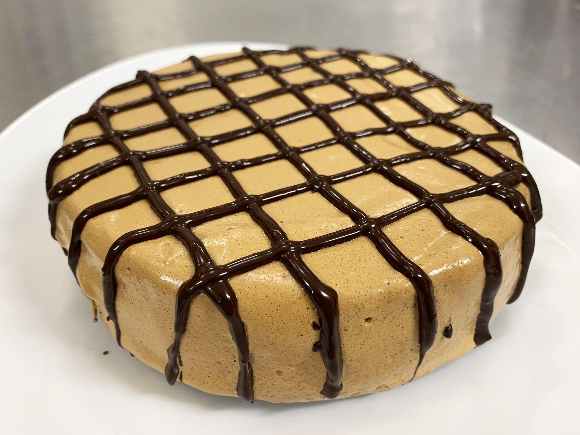 This is a picture of our Dalgona Dark Chocolate Coffee Cake on a white plate, topped with a checkerboard pattern of dark chocolate.