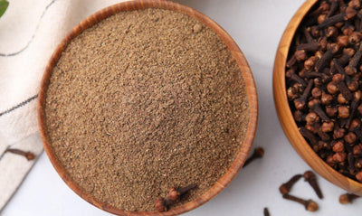 This is a picture of two wooden bowls, one is filled with clove powder and the other on the right is filled with fresh cloves on a white background.