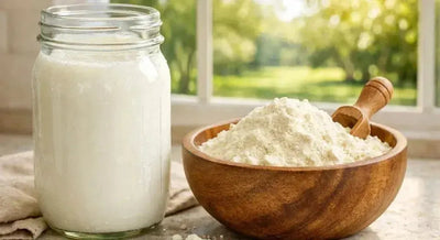 This is a picture of a fresh glass of cold milk next to our whole milk powder in a wooden bowl on a kitchen countertop with a sunny background