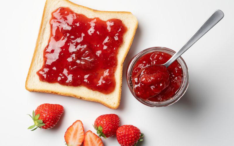 This is a picture of our Homemade Strawberry - Raspberry Jam on fresh bread with a glass bowl on a white background.