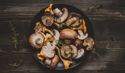 This is a bowl of various mushrooms in a black bowl on a wooden table