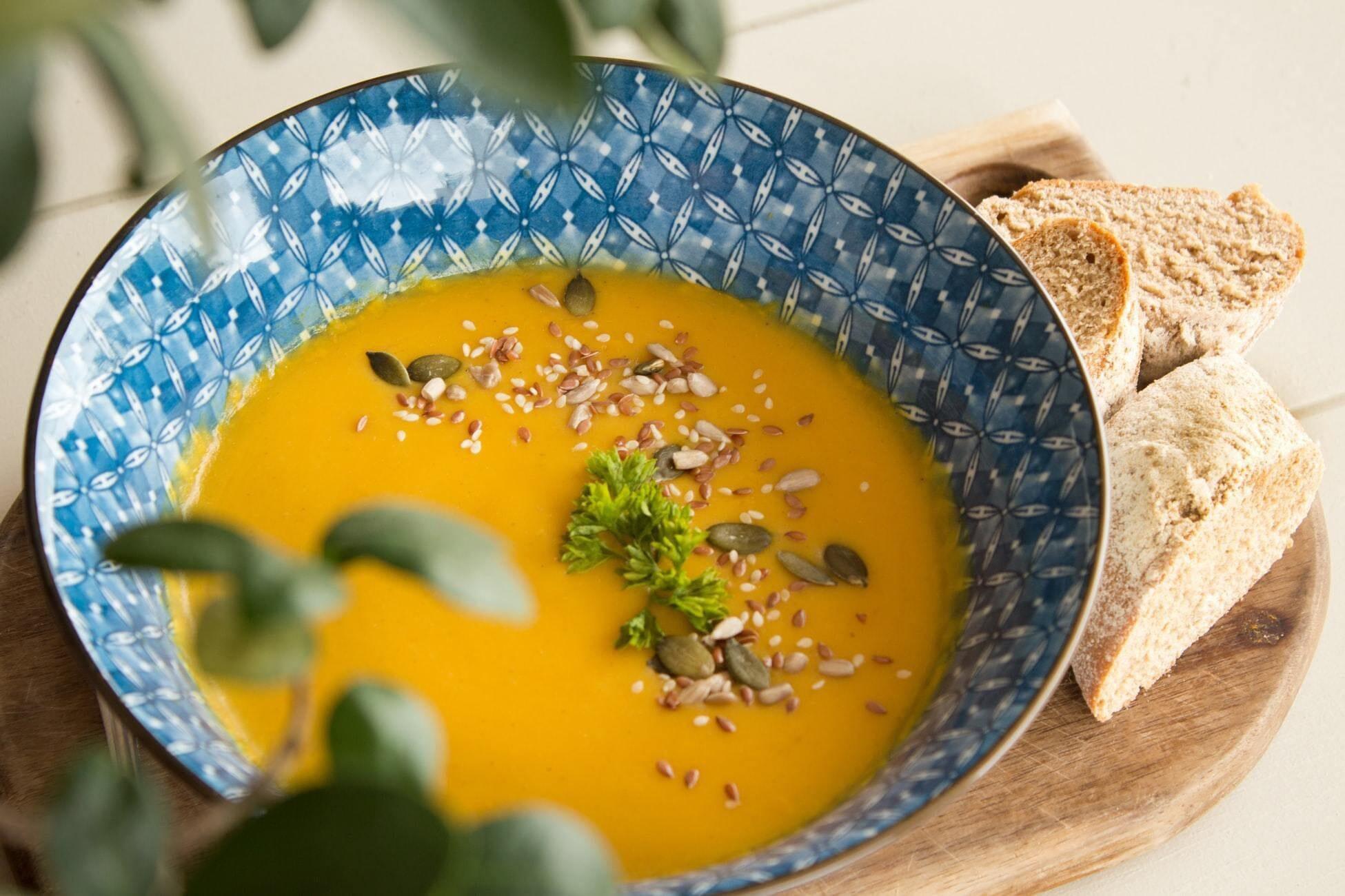 This is a picture of our Organic Pumpkin Soup in a blue bowl on a wooden saucer and slices of bread.