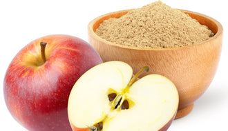 This is a picture of a red apple next to a half apple and a brown bowl of apple powder on a white background.