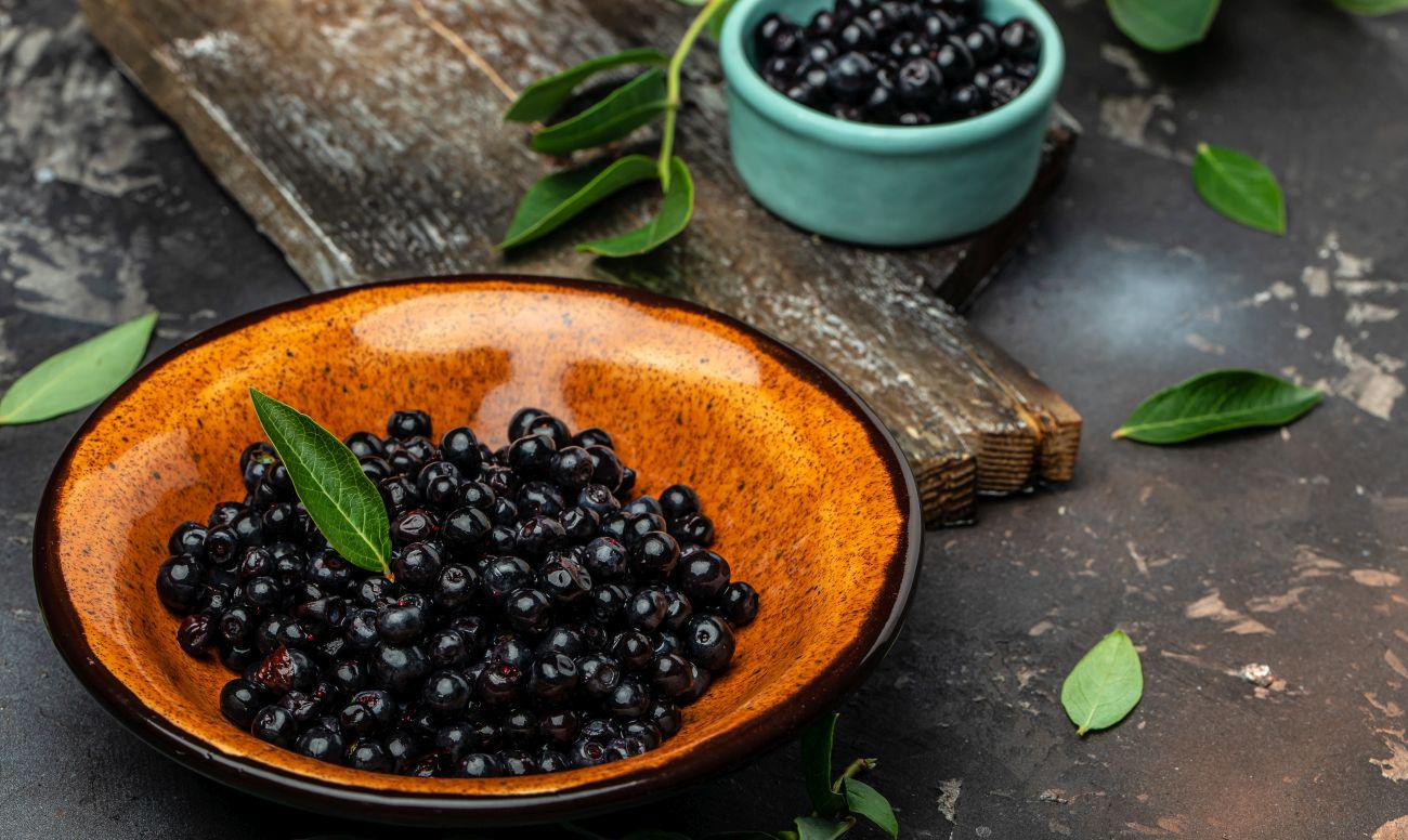 This is a picture of fresh maqui berries in a brown bowl with a small blue bowl of berries on a brown table.