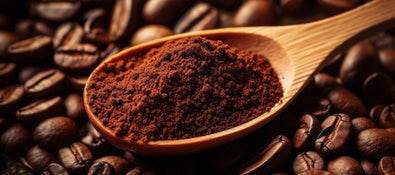 This is a picture of coffee powder on a wooden spoon, on a bed of coffee beans in the background.