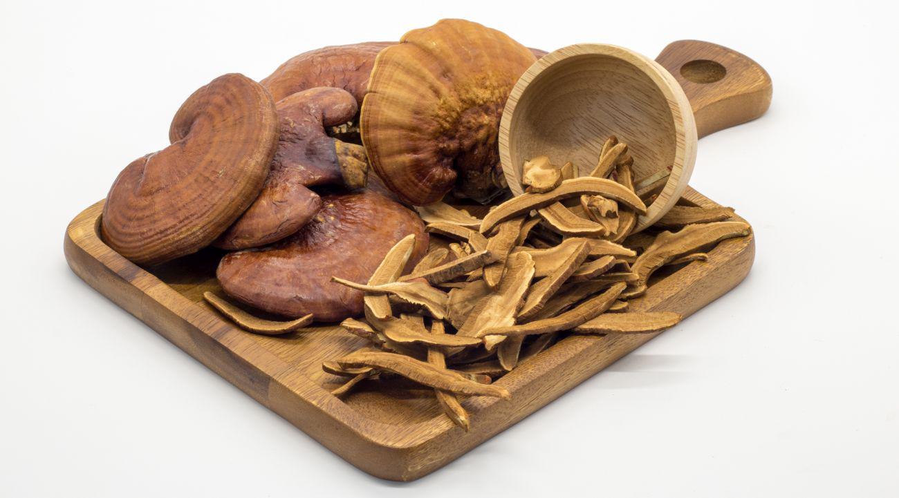 This is a picture of dried red reishi mushroom and pieces on a wooden cutting board on a white background 