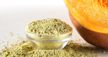 This is a picture of a slice of fresh pumpkin next to a glass bowl filled with pumpkin powder on a white background.