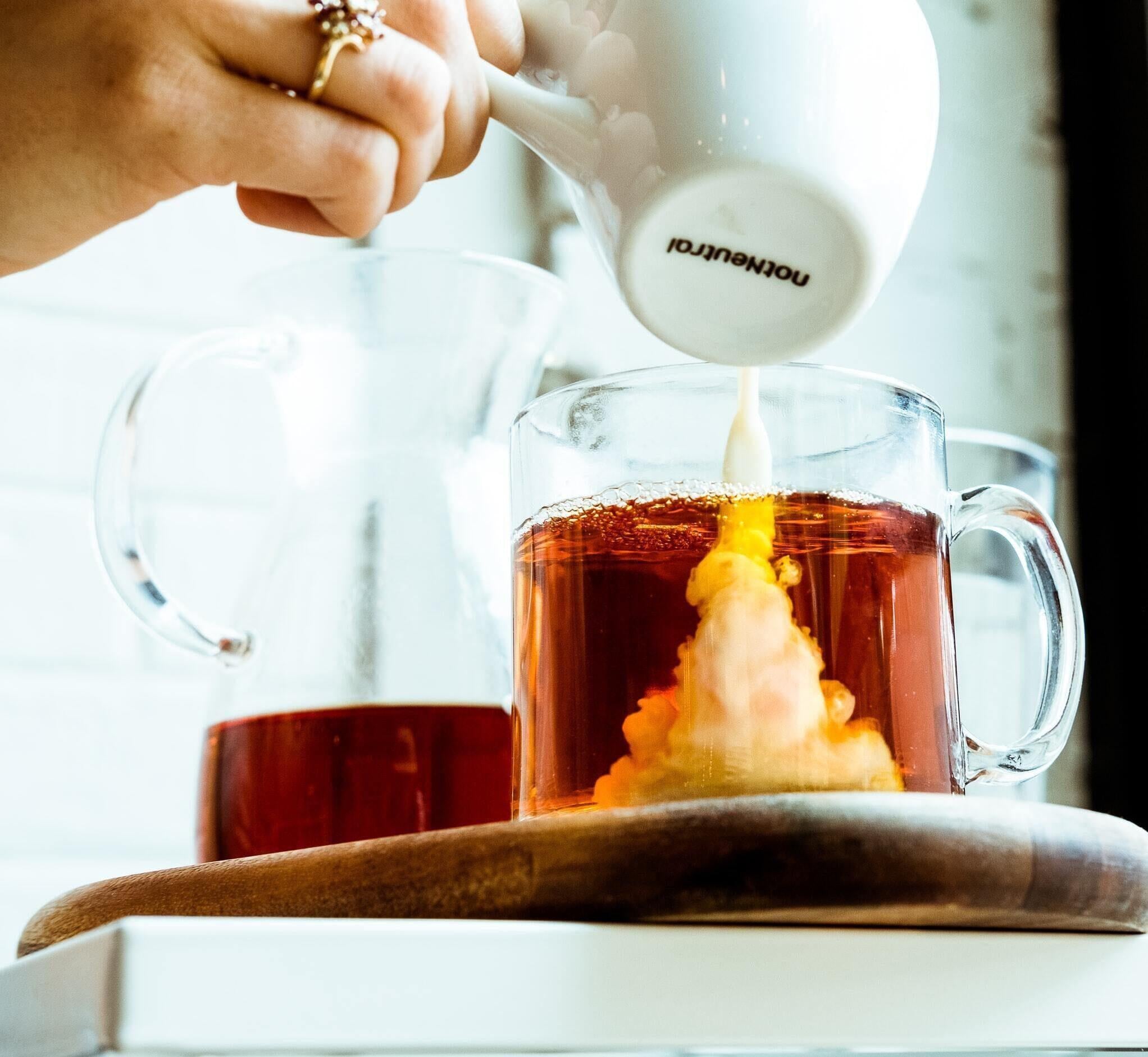 This is a picture of someone pouring creamer into a cup of coffee in a glass mug with a white background.