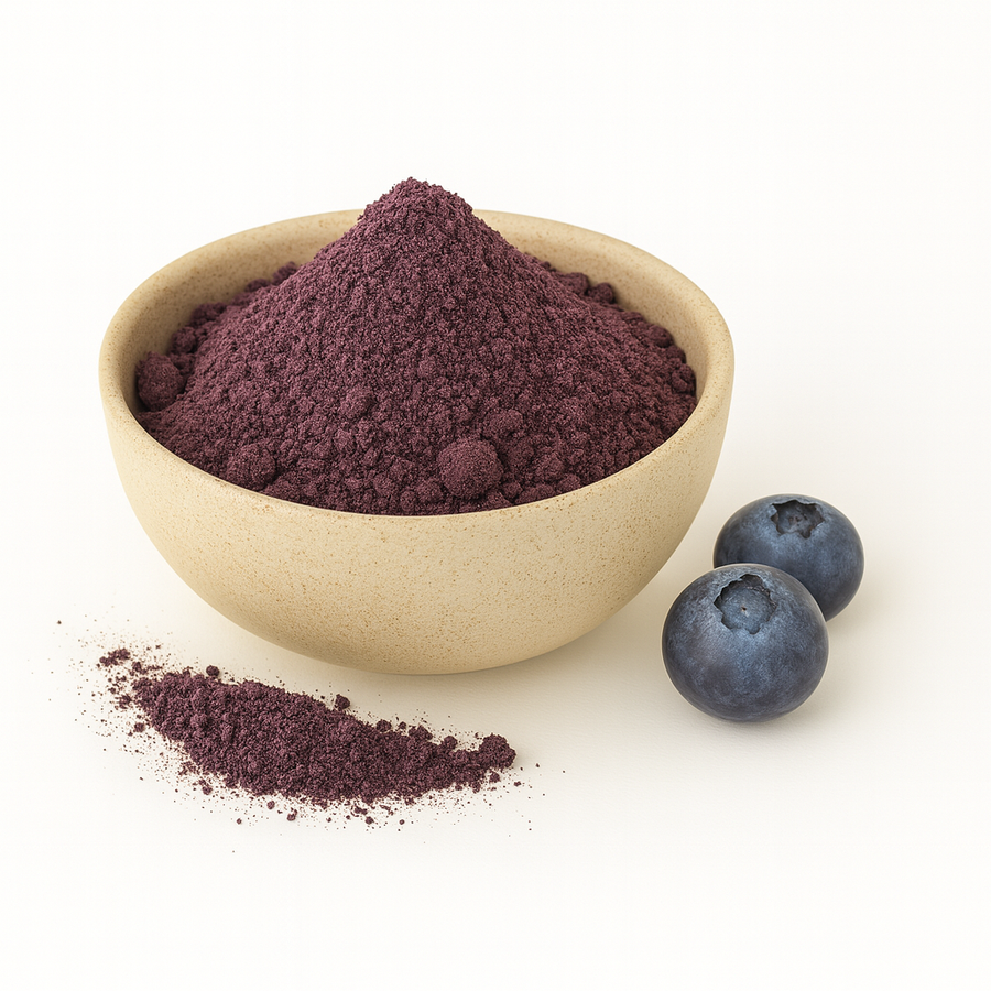 A beige bowl filled with purple blueberry powder on a white background, with a small pile of powder and two fresh blueberries beside it.