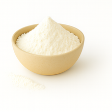 A beige bowl filled with fine white butter powder on a clean white background, with a small amount of powder spilled beside it.