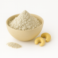 A bowl of cashew nut milk powder with two cashew nuts beside it on a white background.