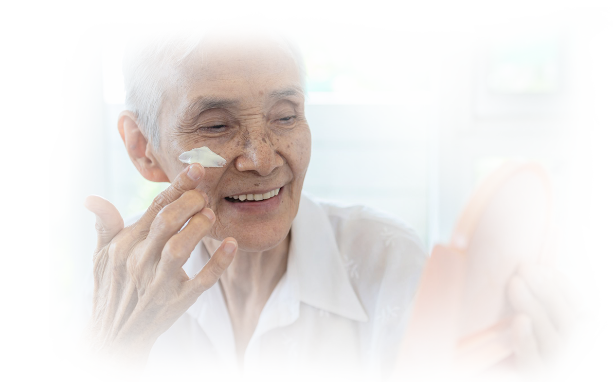 Image of older woman looking into circular mirror applying make-up to conceal age spots.