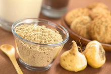 Image of glass bowl containing Maca Root Powder with two yellow maca roots next to it 