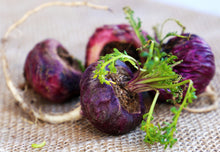 Image of 4 red Maca Roots with stem and leaves on burlap background.