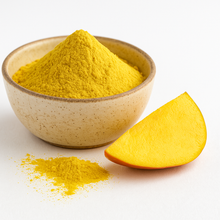 A bowl of organic mango juice powder with a small pile of powder in front and a fresh mango slice beside it on a white background