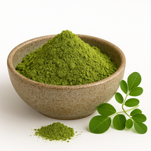 A bowl of organic moringa leaf powder with a small pile of powder in front and a fresh moringa leaf sprig beside it on a white background.