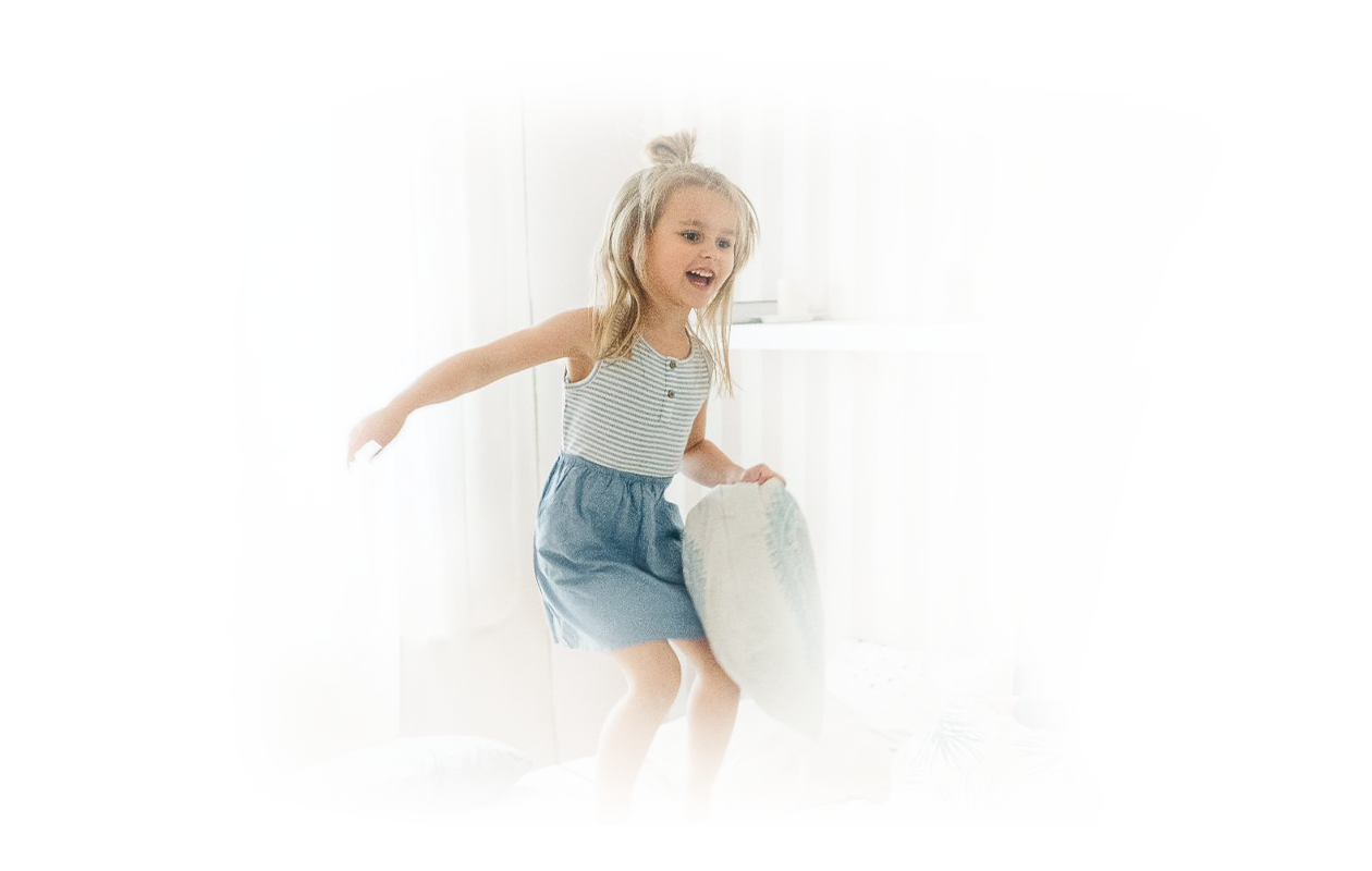 Image of hyperactive young girl jumping up and down having a pillow fight.