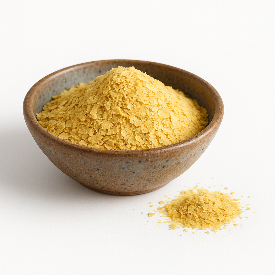 A rustic ceramic bowl with earthy blue speckles filled with organic nutritional yeast flakes, with a small pile of flakes in front on a white background.