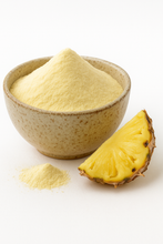A bowl of organic pineapple juice powder with a small pile of powder in front and a fresh pineapple slice beside it.