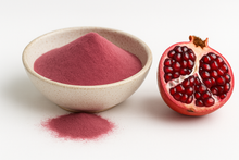 A bowl of bright pink Organic Pomegranate Juice Powder with a small pile spilled in front, next to a halved fresh pomegranate on a white background.