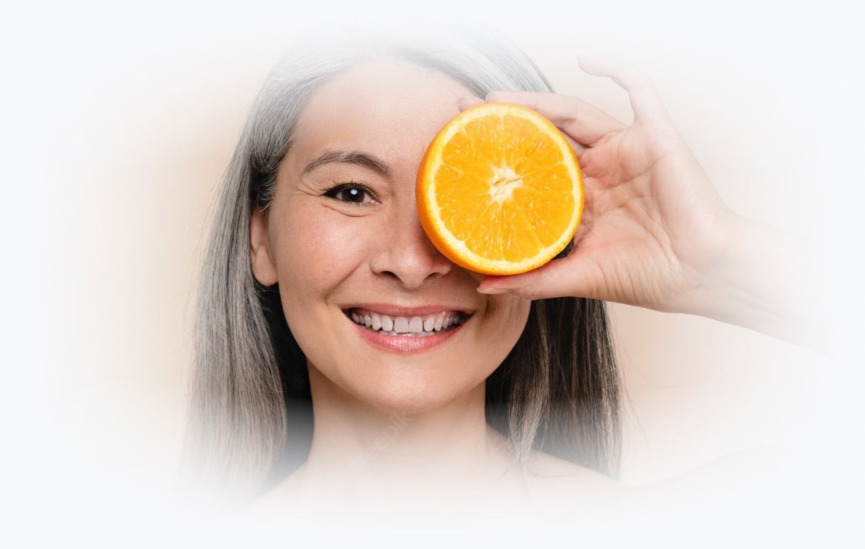 Photo of Woman holding slice of orange to her face covering one of her eyes